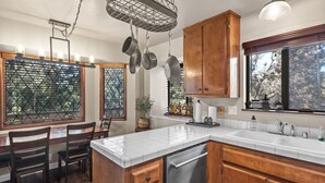 Cocina con armarios de madera, encimera blanca y ollas colgantes.