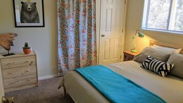 A bedroom with a bed, a nightstand, a dresser, a window with blinds, a door, and a wall with a framed picture.