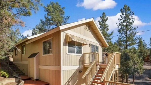 Eine zweigeschossige Holzhütte mit einer Terrasse, Treppe und einem kleinen Balkon.