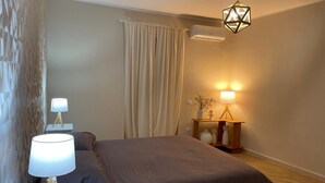A bedroom with a bed, two bedside lamps, a nightstand with a lamp, a wall-mounted air conditioner, and a geometric pendant light. - Goti Rooms B&B (Sant'Agata de'Goti)