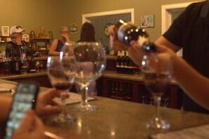 A bar area with multiple wine glasses on the counter, a person pouring a drink, and a variety of bottles in the background.