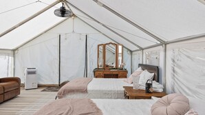 A tented room with two beds, a dresser, a mirror, and a fan.