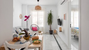 A modern dining area with a wooden table, chairs, and a variety of dishes. There is a potted plant and a hanging light fixture. - Main street free parking 5 minutes away (Nerja)