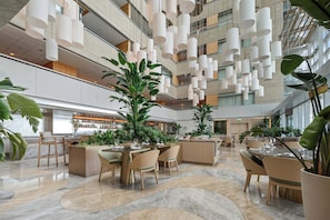 Un'ampia hall d'albergo con diverse zone salotto, un bar e lampade a sospensione.