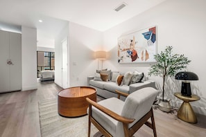A modern living room with a sofa, armchair, round wooden coffee table, and a floor lamp.