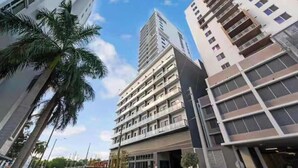 Un immeuble à plusieurs étages doté d’une architecture moderne, comprenant une cour intérieure et un espace de stationnement où sont garées plusieurs voitures.