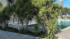 Een zwembadgedeelte met palmbomen en een betonnen gebouw op de achtergrond.