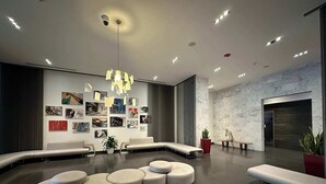 Een moderne lobby met een gebogen zithoek, een muur versierd met diverse foto’s en een marmeren muur met een sculptuur.