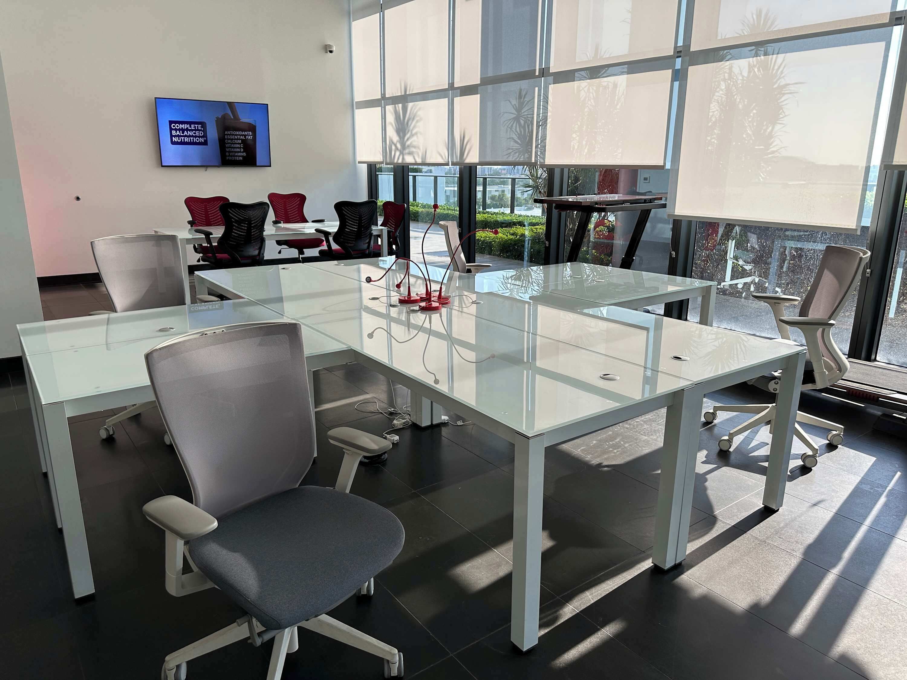 Une salle de conférence moderne, dotée de tables en verre, de chaises de bureau et d’une grande fenêtre offrant une vue sur la verdure et les bâtiments.