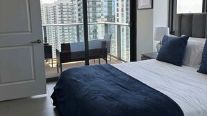 Een moderne hotelkamer met een groot bed, een balkon met uitzicht op hoge gebouwen, een ronde plafondlamp en een kleine tafel met stoelen.