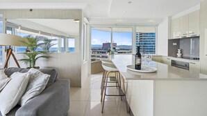 A modern kitchen with a large island, bar stools, and a view of the city. - Spacious 2 Bedroom Ocean View Apartment - Q Stay (Surfers Paradise)