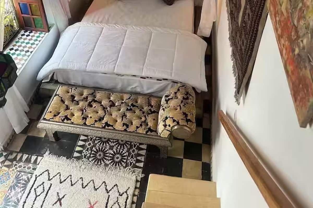 Una camera da letto con un letto, un comodino, un tappeto decorato e una parete con delle opere d'arte.