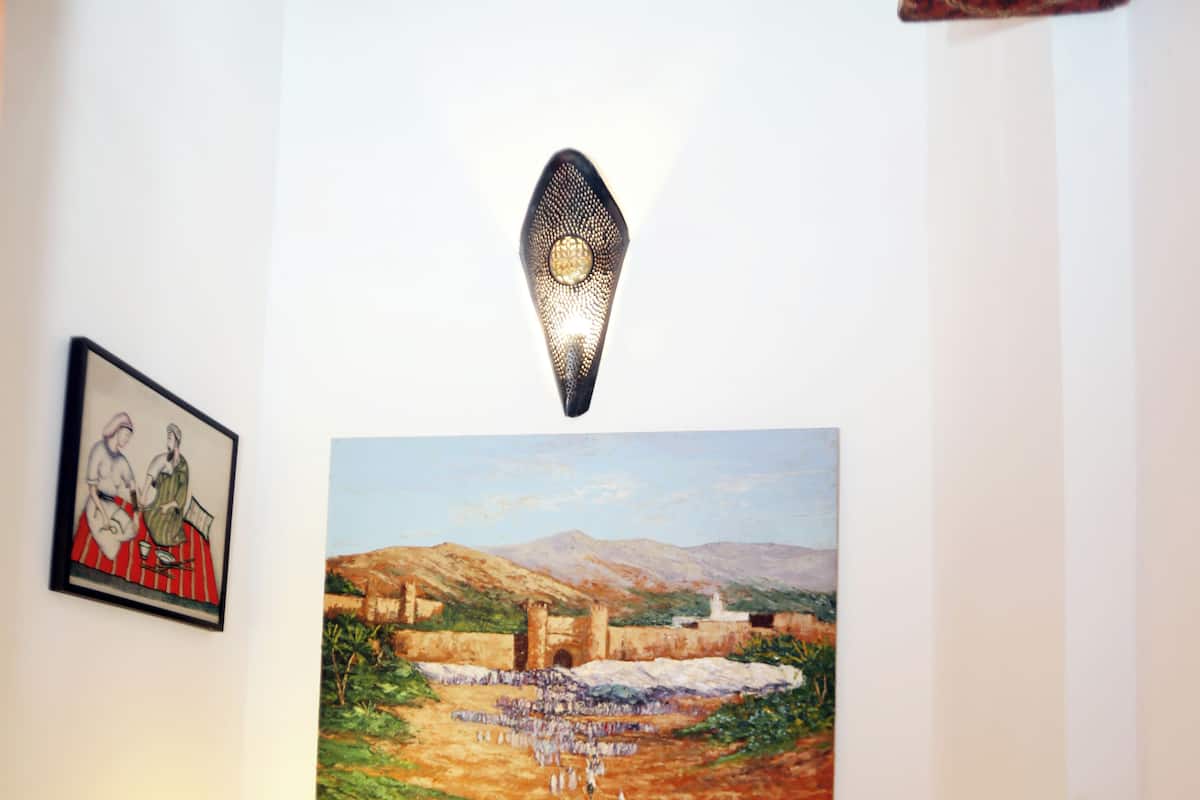 Una camera da letto con un letto, un comodino con una lampada, un quadro incorniciato e un grande dipinto di paesaggio sulla parete.