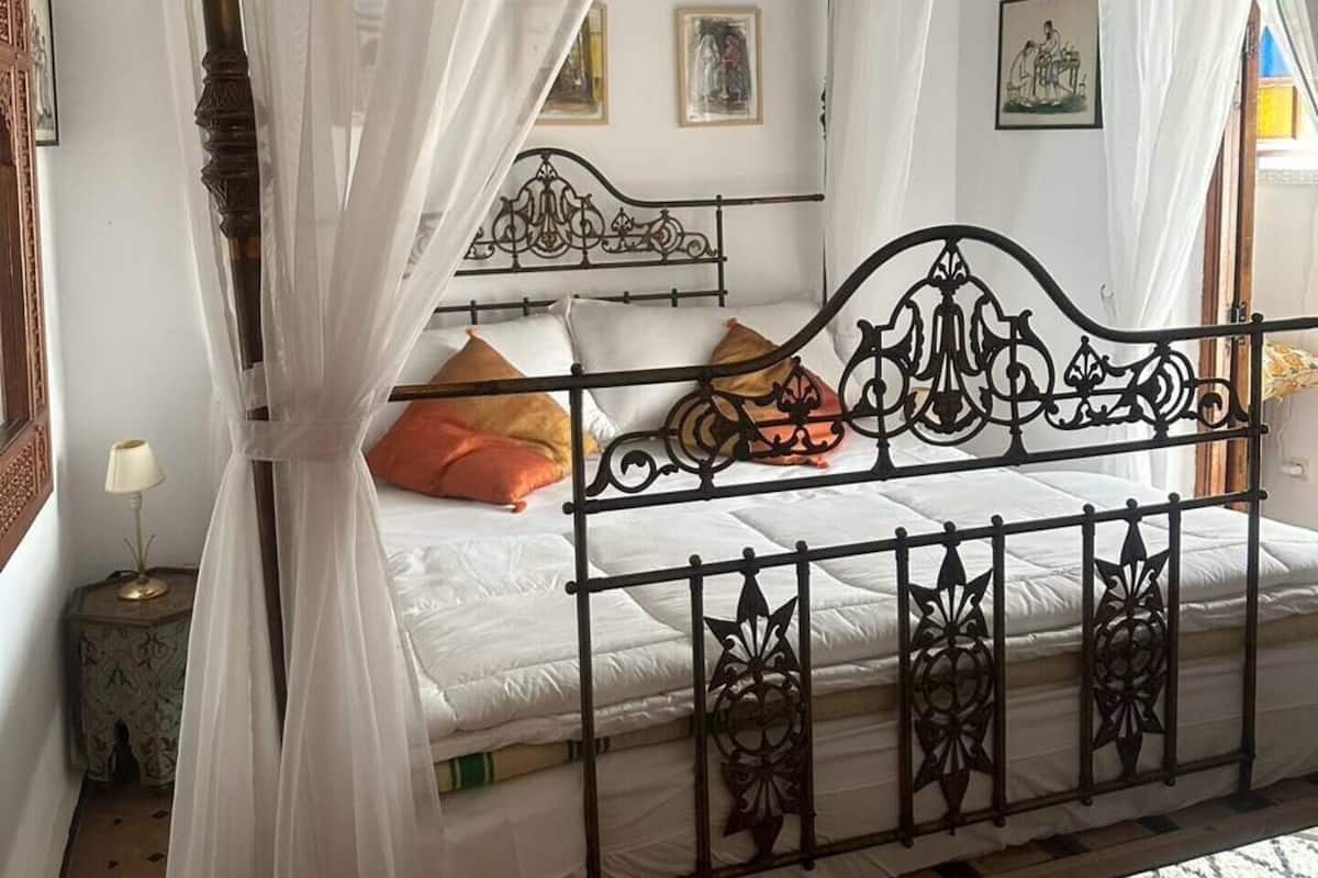 Un letto a baldacchino con tenda, una testiera in metallo decorata e un pavimento piastrellato.