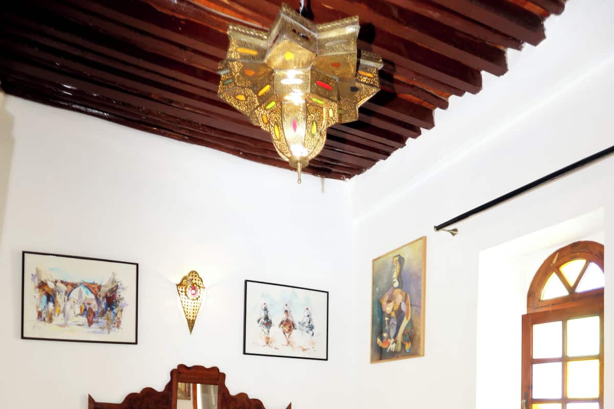 Una camera da letto con un letto grande, una testiera in legno e un lampadario. Si vedono opere d'arte incorniciate alle pareti e una finestra con vista.