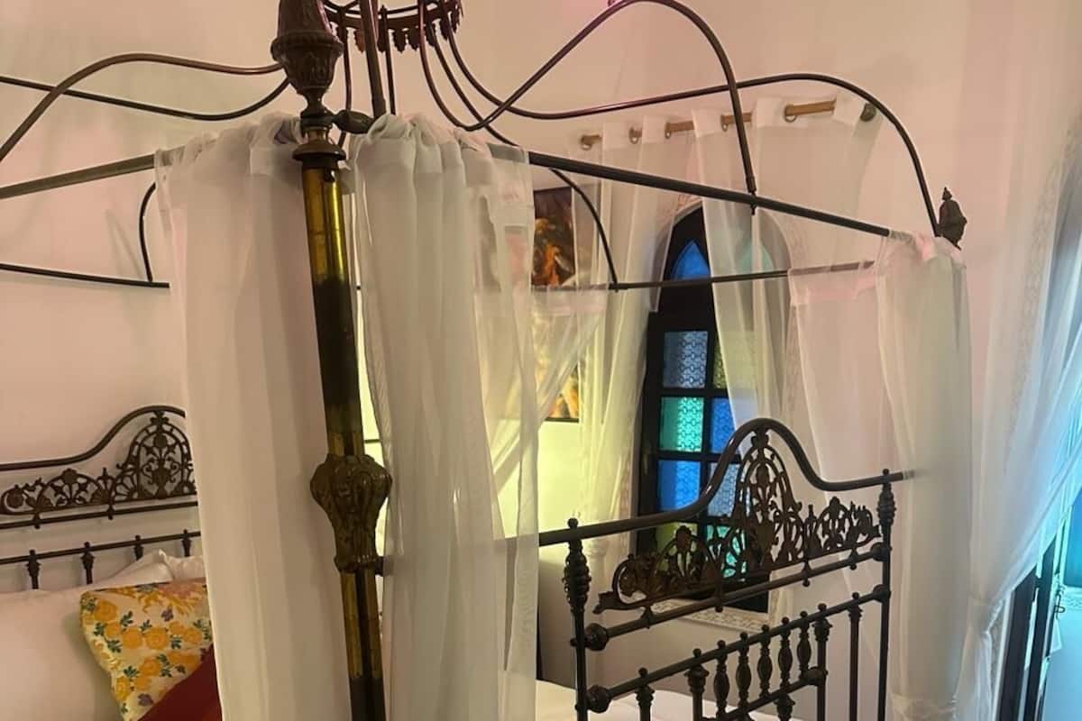 Un letto a baldacchino con tenda, un comodino e una finestra con decorazioni in vetro colorato.