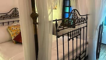 Un llit amb cortines, una tauleta de nit i una finestra amb un disseny de vitrall.