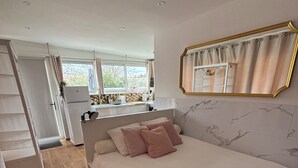 A bedroom with a bed, a dresser, a mirror, and a view of the kitchen. - Charming Independent Studio (La Motte-d'Aigues)
