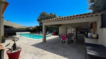 A covered patio area with a pool, outdoor seating, and a kitchen area.