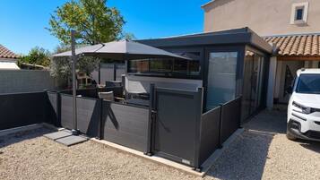 Un espace extérieur moderne, aménagé pour se détendre, avec un patio couvert, une zone délimitée par une clôture et un véhicule garé à proximité.