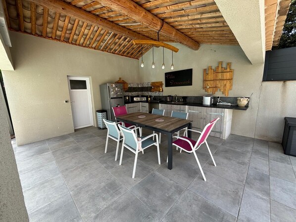 A kitchen with a wooden ceiling, a dining table with chairs, and a refrigerator.