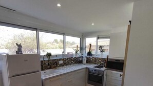 A modern kitchen with white cabinets, a built-in oven, and a large window offering a view of the outdoors. - Charming Independent Studio (La Motte-d'Aigues)