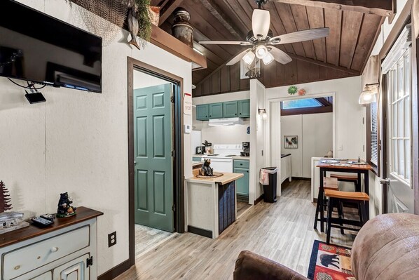 A compact kitchen with a ceiling fan, a dining area with a table and chairs, and a small island with a cat figurine.