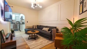 A modern living room with a sofa, coffee table, and a plant. There is a kitchen visible in the background. - Entire apartment, Boston in 14min, Beach in 4min! (Revere)
