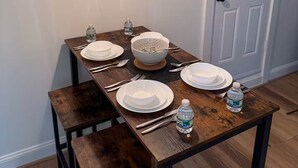 A dining table set with plates, bowls, cutlery, and water bottles, with a pendant light above. - Entire apartment, Boston in 14min, Beach in 4min! (Revere)