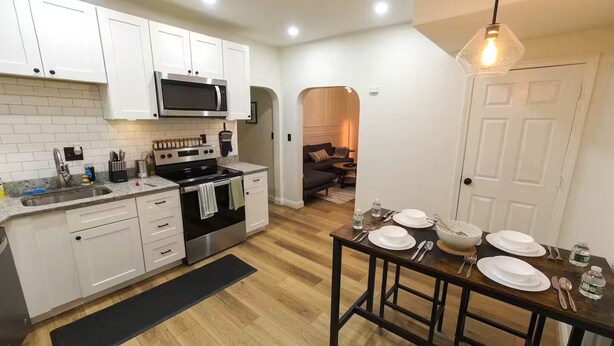 A modern kitchen with white cabinets, a stainless steel stove, and a dining area set for a meal. - Entire apartment, Boston in 14min, Beach in 4min! (Revere)