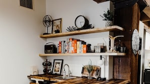 Een keuken met een houten keukeneiland, zwarte barkrukken en planken met boeken en keukengerei.