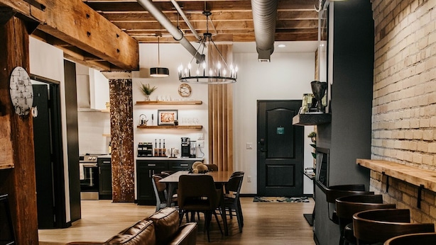 Een modern interieur met een houten plafond, een bar met krukken, een zithoek met een bank en een keuken op de achtergrond.