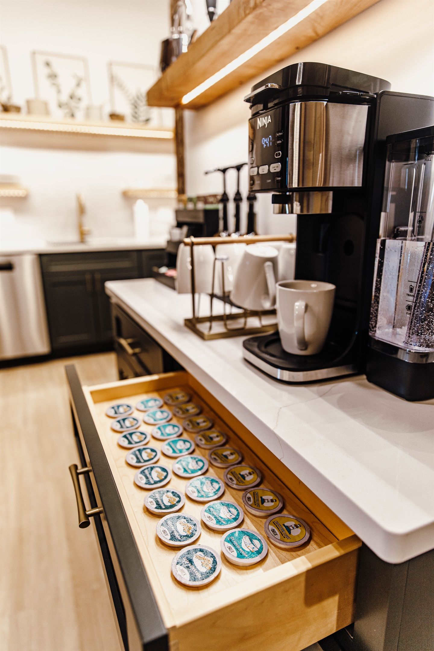 Una cocina con cafetera, un cajón de cápsulas de café y una taza sobre la encimera.