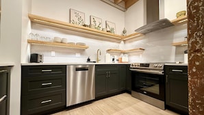 Een moderne keuken met donkere kastjes, roestvrijstalen apparatuur en houten planken.