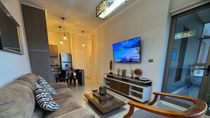 A modern living room with a sofa, a wooden chair, a TV, and a kitchen in the background. - Patagua (Antofagasta)