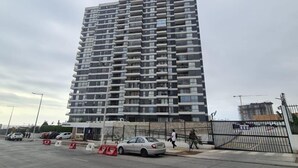 A high-rise residential building with multiple balconies, a gated entrance, and a parking area with cars. - Patagua (Antofagasta)
