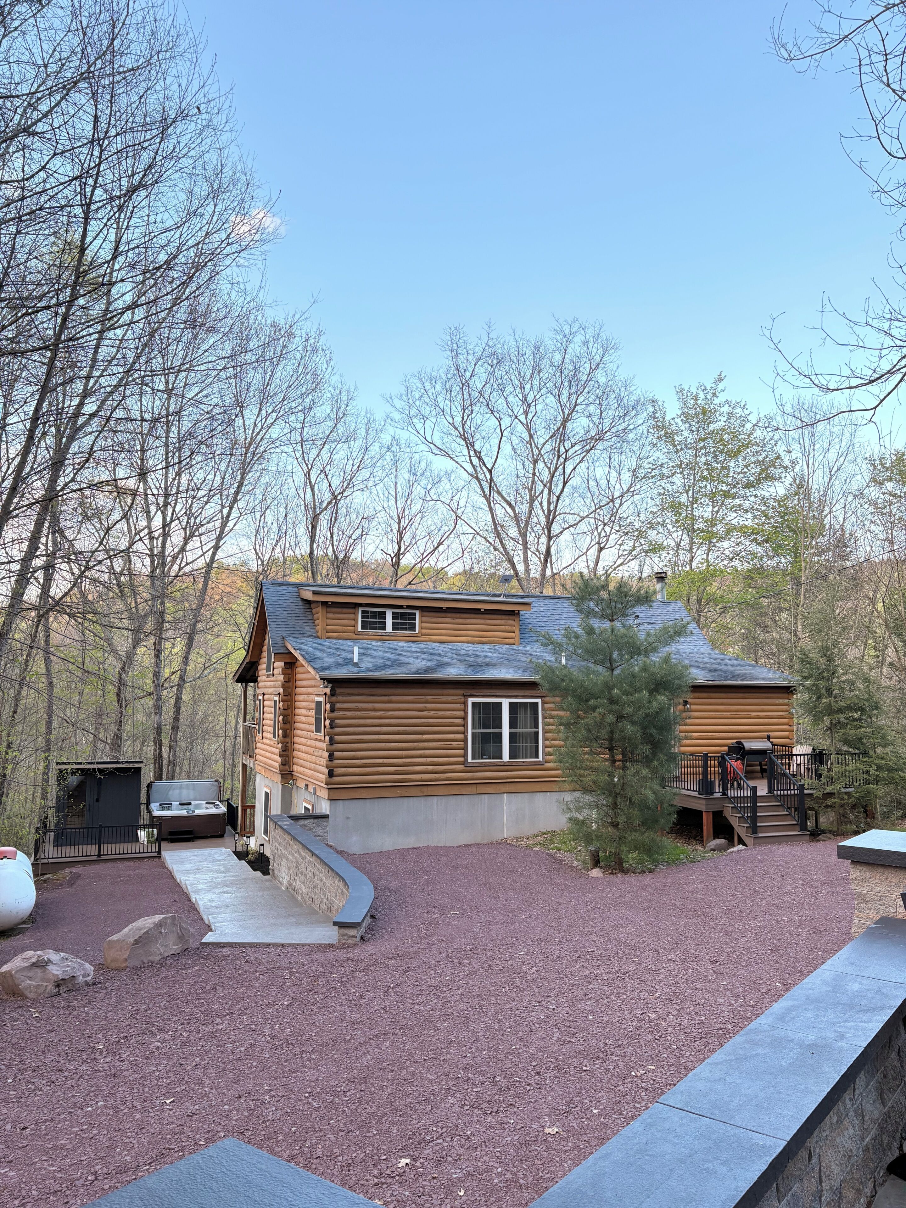 A log cabin with a deck, a barbecue grill, and a small shed.