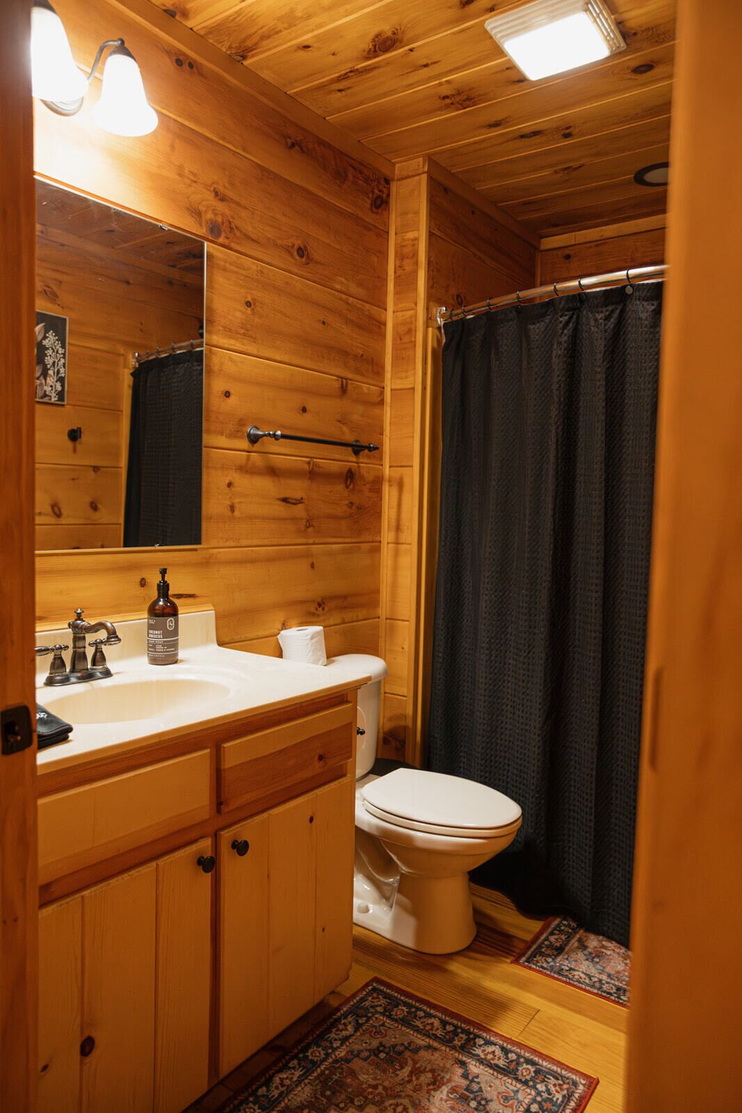 Bagno di una baita in legno con lavandino, wc e tenda per la doccia.