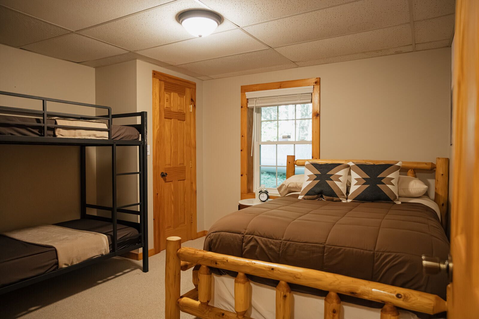 A bunk bed room with a wooden headboard, a window with a view, and a bedside table with a clock.