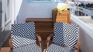 Ein Balkon mit zwei gemusterten Stühlen, einem Holztisch und Blick aufs Meer.