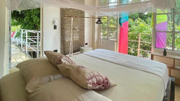A bedroom with a canopy bed, large windows, and a view of greenery outside. - JUMANJI  (Palomino)