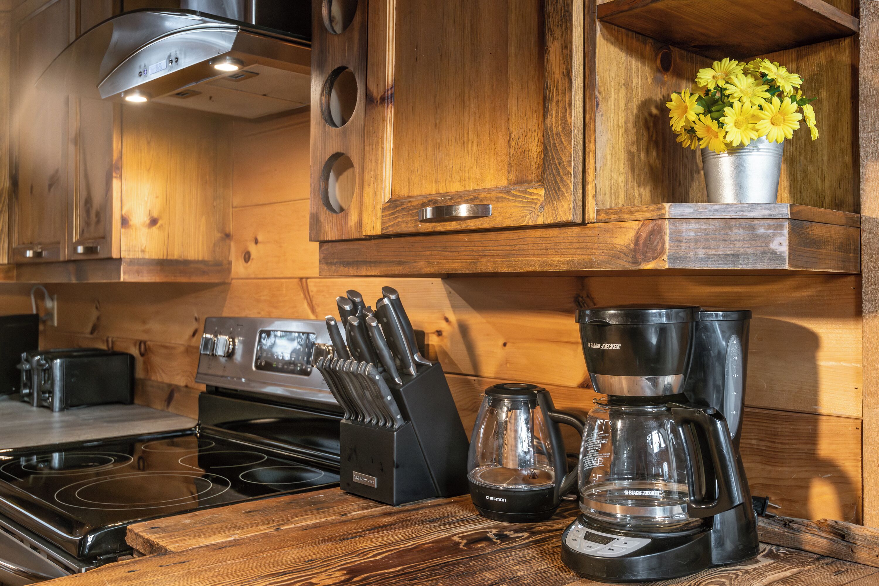 A kitchen with wooden cabinets, a stove, a coffee maker, and a knife block.