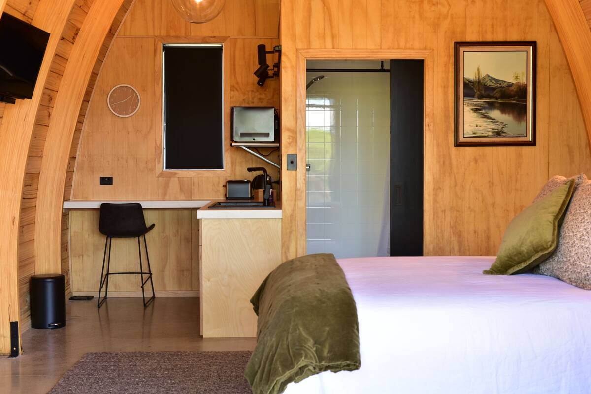 Ein gemütliches Zimmer mit einem Bett, einem Schreibtisch mit Stuhl, einer kleinen Küchenzeile und einer Tür zum Badezimmer.