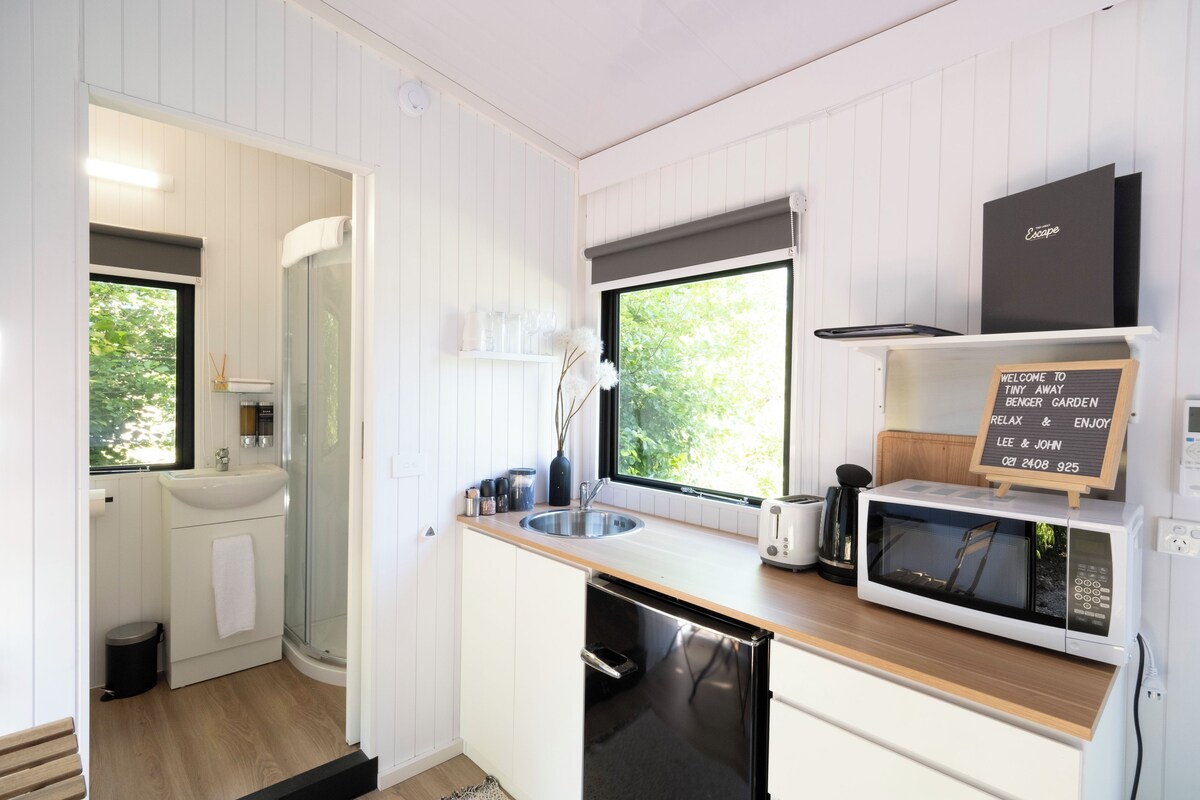A compact kitchen with a sink, microwave, and toaster. A chalkboard sign with contact information is visible.
