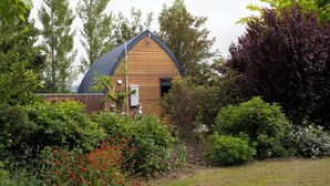 A wooden house with a dark roof, surrounded by lush greenery and flowering plants. - Benger Garden Cafe & Chalets (Ettrick)