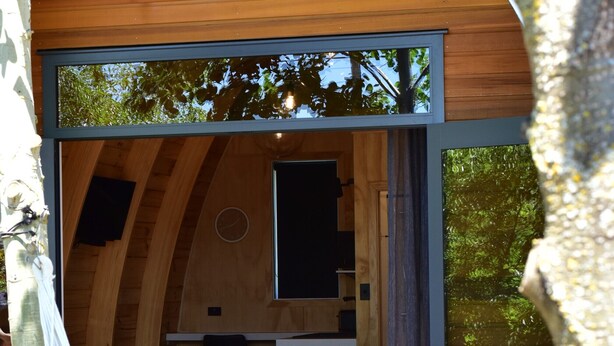 A cozy wooden cabin with a hammock, a small dining area, and a bed. - Benger Garden Cafe & Chalets (Ettrick)