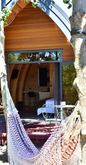 A cozy wooden cabin with a hammock, a small dining area, and a bed. - Benger Garden Cafe & Chalets (Ettrick)