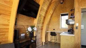 A cozy wooden cabin with a kitchen area, a dining table, and a TV mounted on the wall. - Benger Garden Cafe & Chalets (Ettrick)