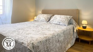 Ein ordentlich bezogenes Bett mit floralem Überwurf, einer Nachttischlampe und einem Nachttisch.