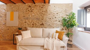Ein gemütliches Zimmer mit Steinwand, Holzbalkendecke, einer Couch mit Kissen, einer Pflanze und einem gerahmten Bild an der Wand.